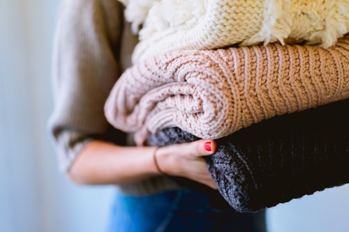 kvinde holder strikkede bluser i tre forskellige farver foran en hvid baggrund