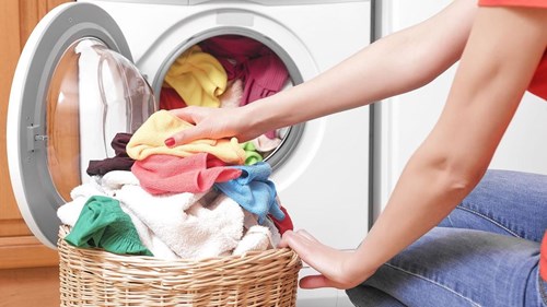 kvinde putter farverigt tøj i vaskemaskinen